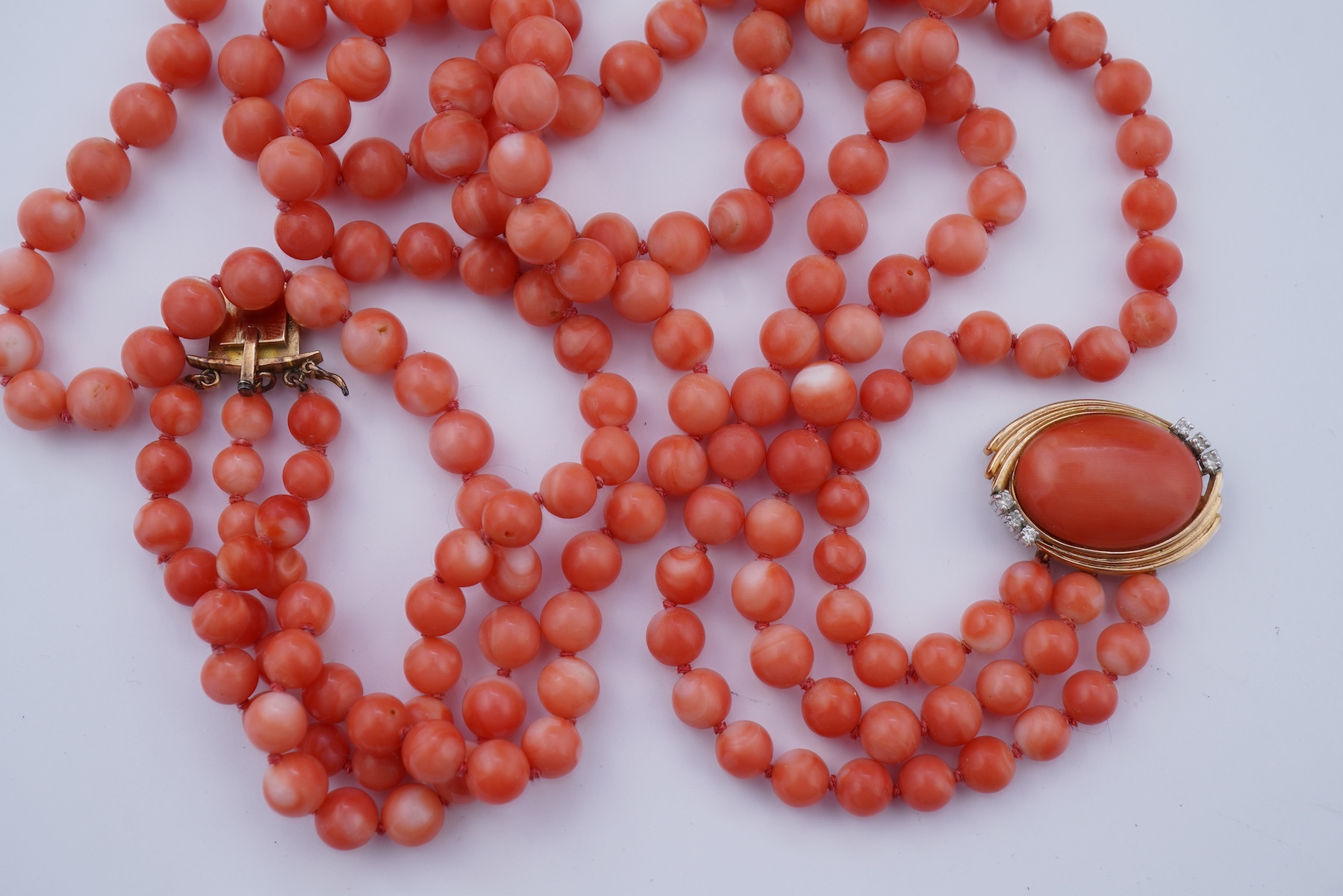 A coral necklace, composed of three strands of coral beads measuring approximately 5.1-6.6mm diameter, to a gold clasp set with a coral cabochon and brilliant-cut diamonds, mounted in gold, length 45.5cm, stamped 14K, ca